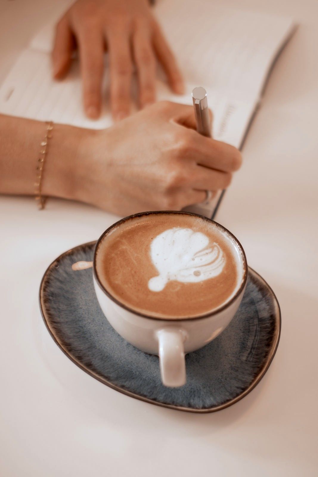 Hände schreiben in ein Notizbuch neben einem Cappuccino